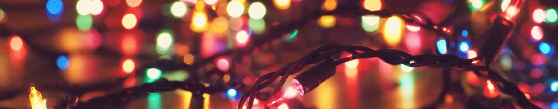 A strand of small multicolored twinkle lights in front of blurred multicolored lights at Christmas