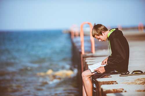 Boy Reading While Sitting on Pier