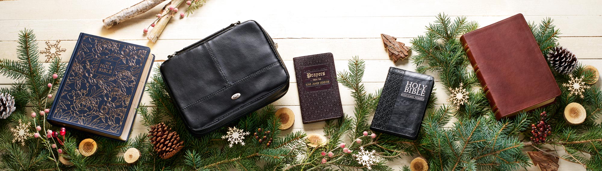 Assortment of Bibles and a Bible cover laying on top of evergreen branches and. Christmas props